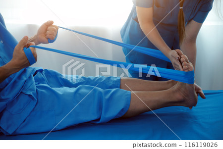 Professional orthopedist examining the little patient's leg in the clinic. Patient at the physiotherapy doing physical exercises with his therapist 116119026