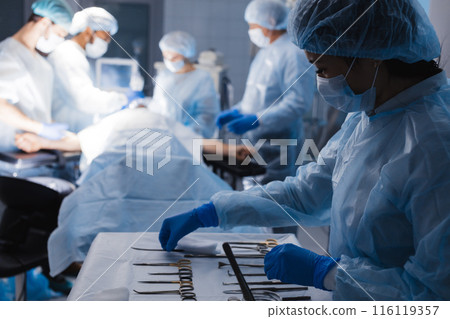 Surgical tools lying on table with nurse near and surgeons at background. 116119357