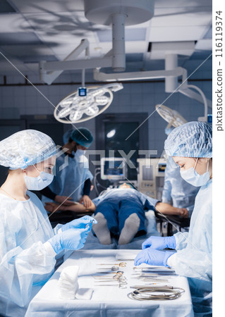 Surgical tools lying on table with nurse near and surgeons at background. Surgical tools lying on table with nurse near and surgeons at background. 116119374