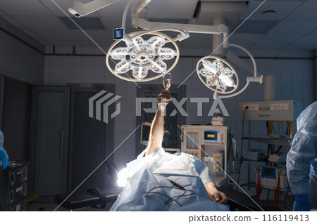 Ironic picture of patient on surgery couch raises up the hand with champagne 116119413