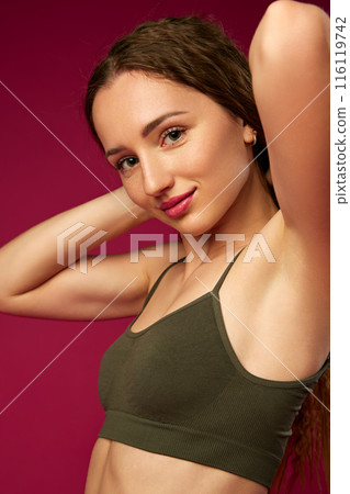 Portrait of attractive young woman with smooth, well-kept skin and nude makeup, posing in green underwear against magenta studio background Portrait of attractive young woman with smooth, well-kept skin and nude makeup, posing in green underwear against magenta studio background 116119742
