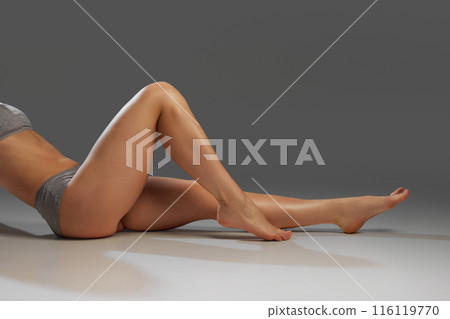 Cropped image of slender smooth female legs against grey studio background. Female model with slim fit body 116119770
