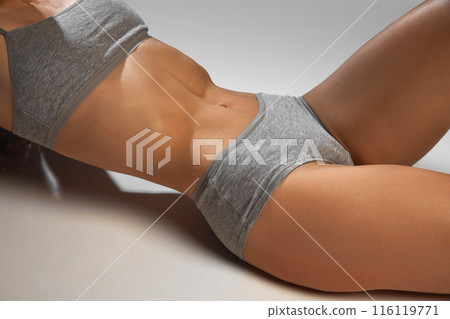 Cropped close-up image of female slim body in underwear against grey studio background. Perfect blend of fitness and natural elegance 116119771