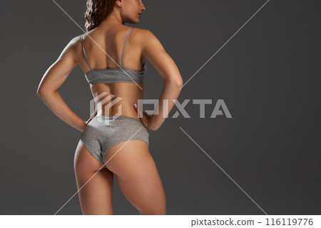 Rear view of cropped female body, young model showing her healthy and fit body, smooth buttocks and relief back against grey studio background 116119776