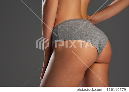 Cropped image of female buttock in cotton underwear against grey studio background. Comfortable lingerie, fit smooth body Cropped image of female buttock in cotton underwear against grey studio background. Comfortable lingerie, fit smooth body 116119779