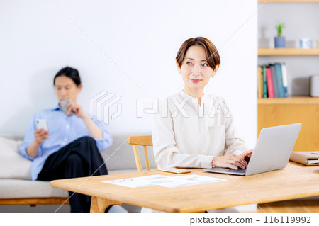 A woman working remotely and a man relaxing on the sofa 116119992