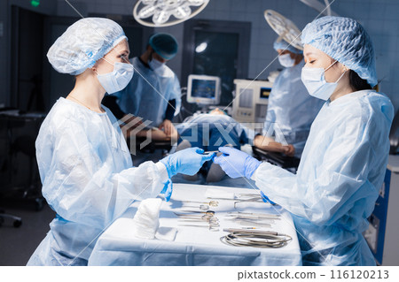 Surgical tools lying on table with nurse near and surgeons at background. Surgical tools lying on table with nurse near and surgeons at background. 116120213