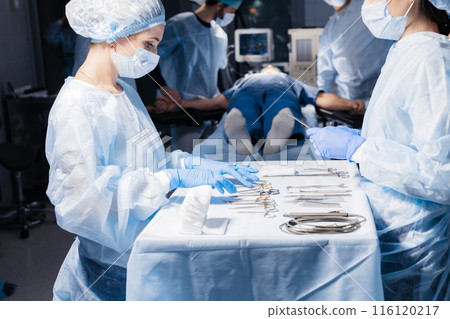 Surgical tools lying on table with nurse near and surgeons at background. 116120217