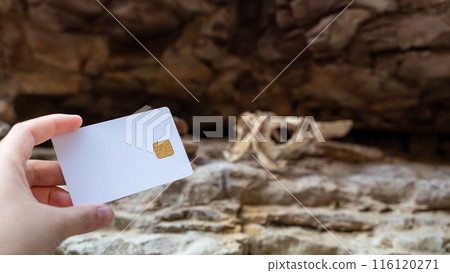 A woman's hand holds a white bank card against a background of a rocky canyon and an animal skull. A woman's hand holds a white bank card against a background of a rocky canyon and an animal skull. 116120271