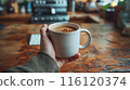 Closeup Of Hand Holding Coffee Mug On Wooden Table In Cafe 116120374