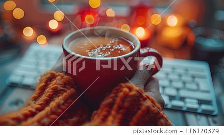 Hands Holding a Red Mug of Hot Drink With Steam in Front of a Computer Keyboard at Night 116120379