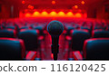 A Single Microphone on a Stage With Red Lights and Empty Seats 116120425