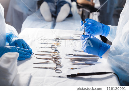 Surgical tools lying on table with nurse near and surgeons at background. Surgical tools lying on table with nurse near and surgeons at background. 116120991
