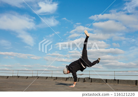 Street dancer hipster guy makes back flip with arm support on the roof outdoor. Street dancer hipster guy makes back flip with arm support on the roof outdoor. 116121220