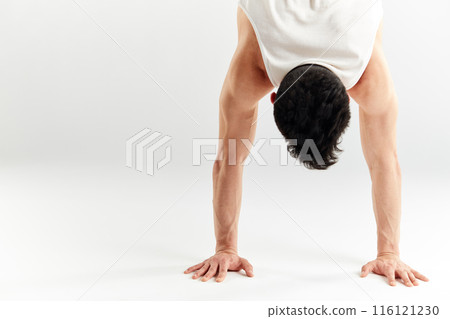 Young man in red sweatpants doing a handstand on hands on white background 116121230