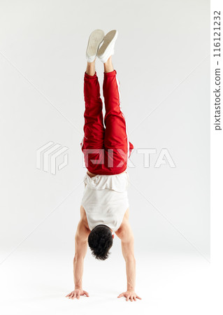 Young man in red sweatpants doing a handstand on hands on white background 116121232