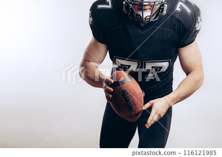 Muscular american football player in protective uniform and helmet holding ball Muscular american football player in protective uniform and helmet holding ball 116121985