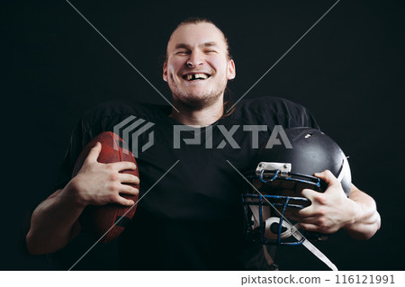 Confident american football player in black sportwear holding helmet and ball 116121991