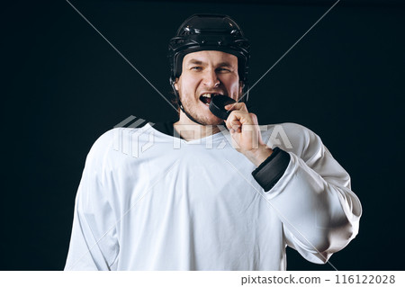 Hockey player bites the puck with broken teeth and looking at camera with a grin. 116122028