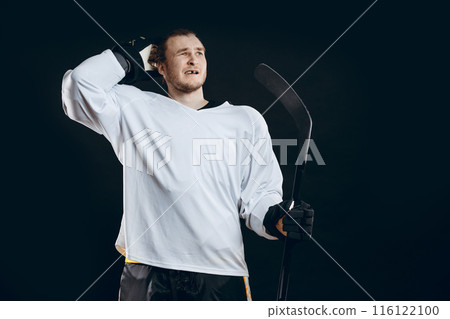 Confused Ice-hockey player standing with hockey stick on black background. 116122100