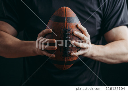 Muscular american football player in protective uniform and helmet holding ball Muscular american football player in protective uniform and helmet holding ball 116122104