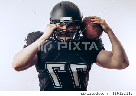 Muscular american football player in protective uniform and helmet holding ball Muscular american football player in protective uniform and helmet holding ball 116122112