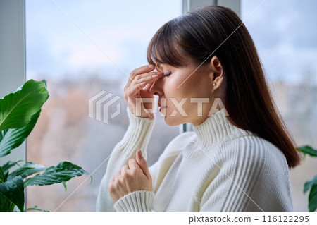 Middle aged woman experiencing headache migraine, at home near window 116122295