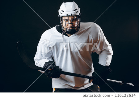 Portrait of ice-hockey player with hockey stick and puck isolated over black 116122634