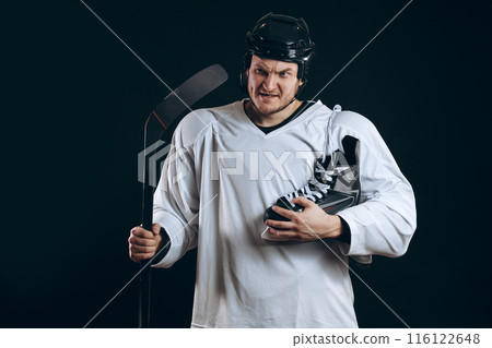 Confident hockey player looking at camera with skate in hand. Isolated on black. 116122648