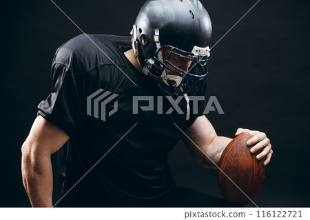 American football player in black sportwear with a ball on black background American football player in black sportwear with a ball on black background 116122721