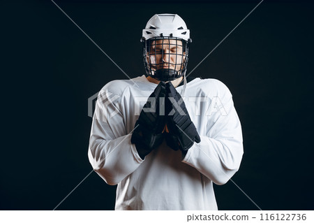 Caucasian hockey player, in uniform, isolated on black, prays for good luck. Caucasian hockey player, in uniform, isolated on black, prays for good luck. 116122736