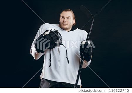 Handsome young man holding hockey stick covers mouth with hand expresses fear 116122740