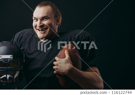 Confident american football player in black sportwear holding helmet and ball Confident american football player in black sportwear holding helmet and ball 116122744