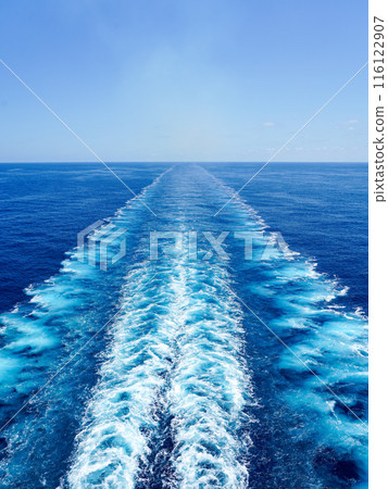 Wide turbulent white foam water trail behind a large cruise ship in a calm blue sea on a sunny day 116122907