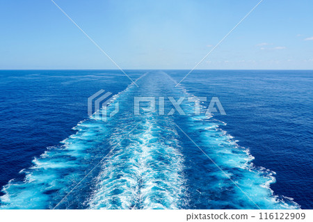 Wide turbulent white foam water trail behind a large cruise ship in a calm blue sea on a sunny day 116122909