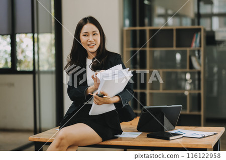 Asian businesswoman talking on phone, using laptop, looking at screen, entrepreneur manager consulting client by call, looking at computer screen, discussing project, reading information 116122958