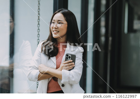 Portrait of a happy Asian businesswoman using mobile phone indoor, Asian businesswoman working in modern office. 116122997