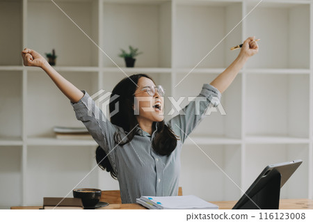 Happy asian woman office worker feeling excitement raising fists celebrates career ladder promotion or reward, businesswoman sitting at desk receive online news, great results successful work concept. 116123008