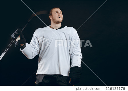 Confused Ice-hockey player standing with hockey stick on black background. 116123176