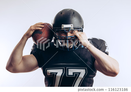 Muscular american football player in protective uniform and helmet holding ball Muscular american football player in protective uniform and helmet holding ball 116123186