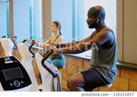 Young biracial couple spending time together in premium fitness club , they doing cardio and man listening to music 116123857