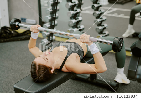 Young active woman lying on leather bench and doing bench press by herself 116123934