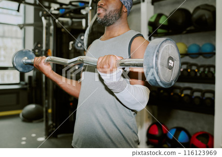 Medium close up of African American man picking up ten kilogram barbell Medium close up of African American man picking up ten kilogram barbell 116123969