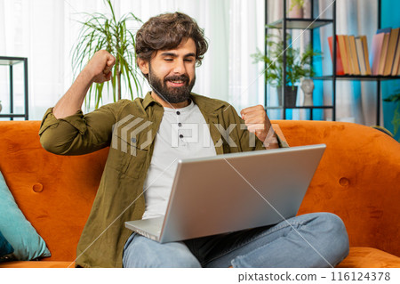 Amazed young man use laptop computer, receive good news message, shocked by victory, celebrate win 116124378