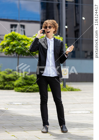 Businessman making phone call online conversation loudspeaker talking waving hello outside office 116124417