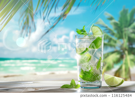 Mojito cocktail with lime wedges and fresh mint in a tall glass on wooden table, tropical beach 116125484
