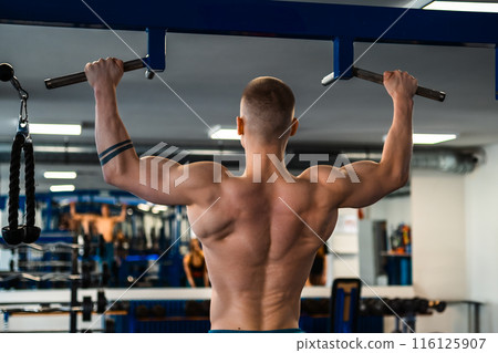 Bodybuilder doing pull-ups in a gym.  116125907