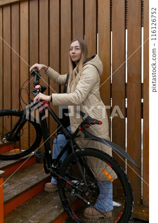 Woman Standing Next to Bike in Front of Wooden Fence Woman Standing Next to Bike in Front of Wooden Fence 116126752