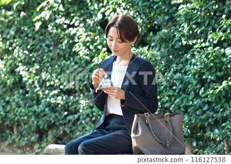 A woman sitting on a bench eating rice balls A woman sitting on a bench eating rice balls 116127538