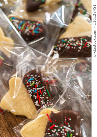 Carefully packaging Christmas cutout cookies, half-dipped in chocolate and presented in clear cellophane wrapping, perfect for festive gifting. Carefully packaging Christmas cutout cookies, half-dipped in chocolate and presented in clear cellophane wrapping, perfect for festive gifting. 116128451